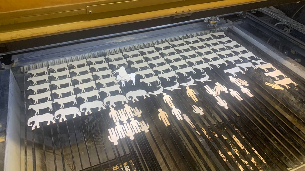 Laserleikkuri työstää pieniä eläin- ja ihmishahmoja koivuvanerista tuotantolinjalla.